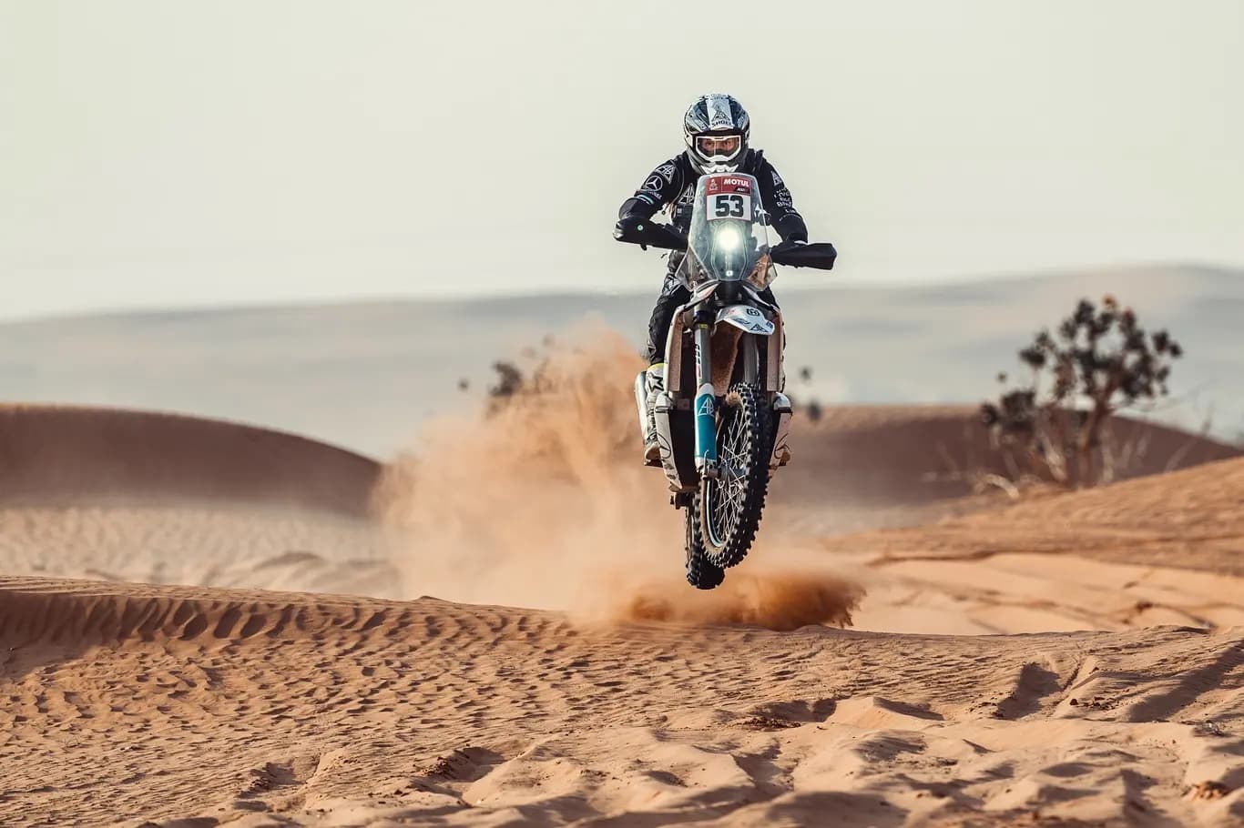 Rally rider jumping over a sand dune, kicking up sand