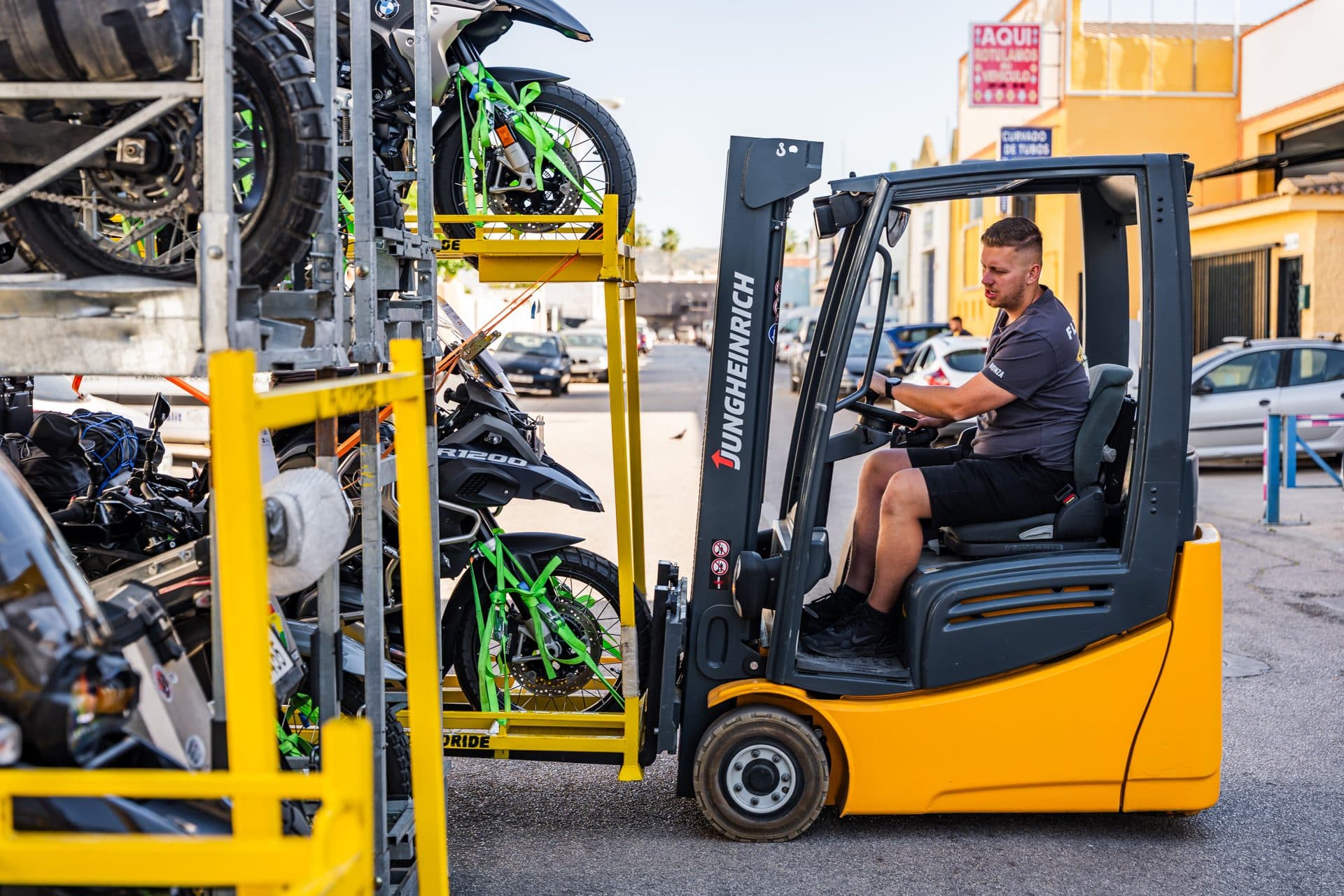 Motorcycles strapped into yellow FLYTORIDE transport cages next to a forklift