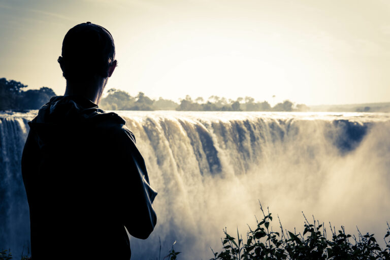 Traveling man observing Victoria Falls, and experiencing the power fo the water falls